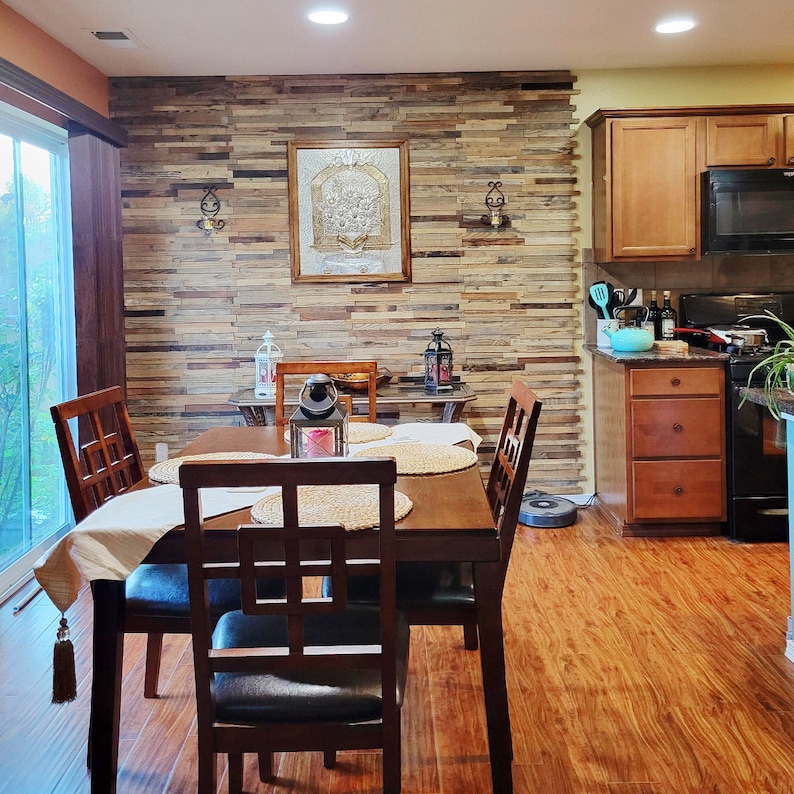 May include: A dining room with a wooden table and chairs. The wall behind the table is covered in wood paneling. There is a framed picture on the wall and a window in the background.