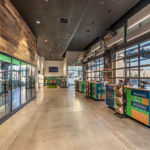 May include: A modern grocery store interior with a wood-paneled wall, glass-door refrigerators, and a checkout counter with a sign that reads "Healthy, Fresh & Affordable Food Made For You".