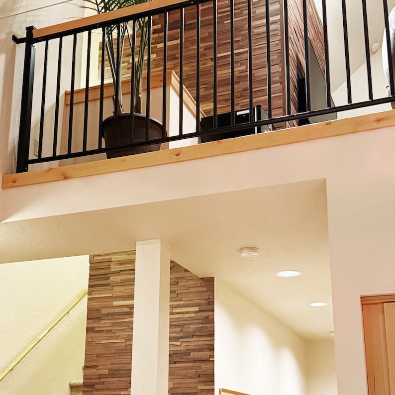 Pu&ograve; includere: Una ringhiera in metallo nero con un corrimano in legno, che si affaccia su una stanza con una parete rivestita in legno e un soffitto bianco. Sono visibili due luci da soffitto bianche.
