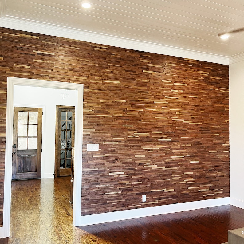 Pu&ograve; includere: Un muro con una parete di accento in legno a pannelli realizzata con assi di legno marrone scuro. La parete &egrave; in una stanza con modanature bianche e un soffitto bianco. Ci sono due porte sullo sfondo.