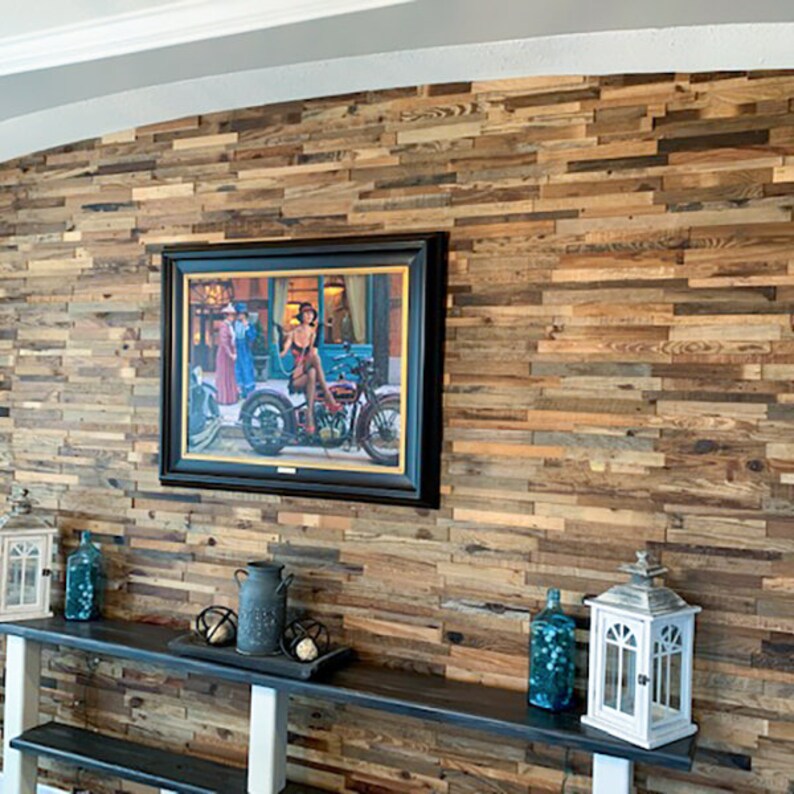 May include: A rustic wood wall paneling with a dark wood shelf and decorative items, including a framed picture of a woman on a motorcycle, a lantern, and a glass bottle.
