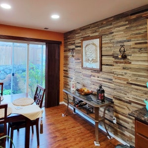 May include: A dining room with a wood-paneled accent wall, a glass-top table with two chairs, and a console table with a glass top and a metal frame. The console table has a wine rack and a decorative bowl on top.