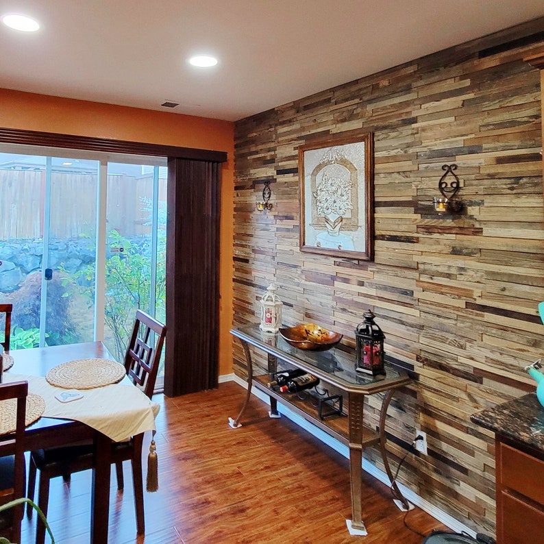 May include: A dining room with a wood-paneled accent wall, a glass-top table with two chairs, and a console table with a glass top and a metal frame. The console table has a wine rack and a decorative bowl on top.