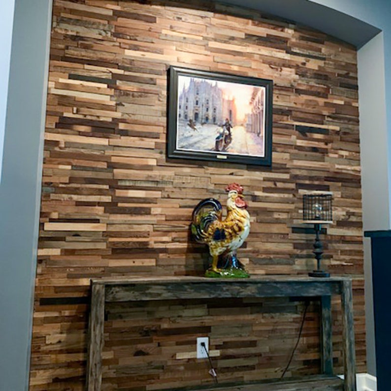 May include: A rustic wooden wall with a distressed finish, featuring a framed picture of a cityscape and a ceramic rooster figurine on a wooden console table. The table has a weathered finish and a black lamp with a wire cage shade.