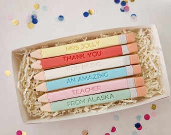 Könnte beinhalten: Eine Schachtel mit sechs dekorierten Zuckerkeksen in Form von Bleistiften. Jeder Keks ist mit einer anderen Farbe glasiert und hat eine darauf geschriebene Botschaft. Die Botschaften lauten: "Mrs. Jolly", "Danke", "Für Dass Du", "Eine Unglaubliche", "Lehrerin", und "Aus Alaska".