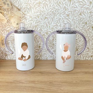 May include: Two white stainless steel sippy cups with clear handles and lids. The cups have a cartoon image of a baby on each side. One cup says "Louis" and the other says "Emma".