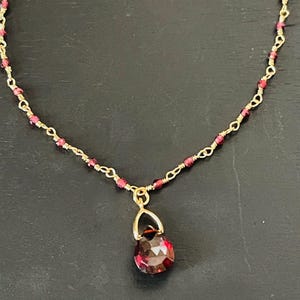 Puede incluir: Un delicado collar de cadena dorada con peque&ntilde;as cuentas rojas y un colgante de piedra roja.