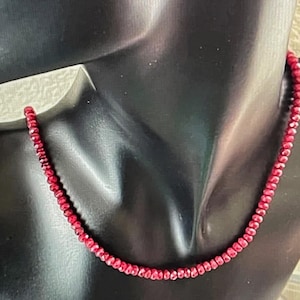 May include: A red gemstone necklace with small, faceted beads. The necklace is on a black mannequin.
