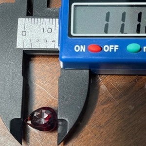 Puede incluir: Una piedra preciosa roja en forma de l&aacute;grima que se mide con un calibre digital. El calibre muestra 11 mm.