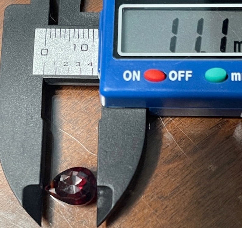 Puede incluir: Una piedra preciosa roja en forma de l&aacute;grima que se mide con un calibre digital. El calibre muestra 11 mm.