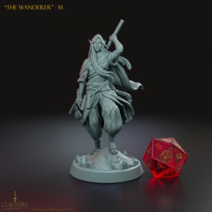 Könnte beinhalten: Eine graue Harzminiatur mit der Aufschrift THE WANDERER - M, die eine kapuzentragende, elfenartige Figur in geschichteten Gewändern mit einem Stab darstellt. Die Figur steht auf einem runden Sockel neben einem transparenten roten zwanzigseitigen Würfel.