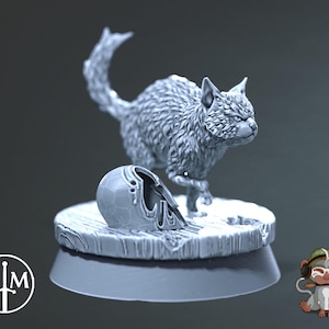 Könnte beinhalten: Eine graue, pelzige Katzenfigur mit einem zerbrochenen Helm zu ihren Füßen. Die Katze steht auf einem grauen, runden Sockel mit einer strukturierten Oberfläche.