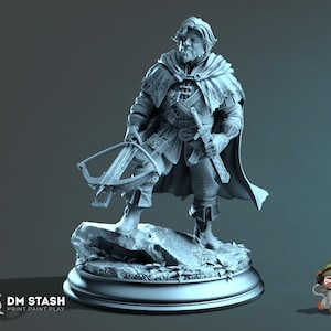 Könnte beinhalten: Eine graue Harzminiaturfigur eines bärtigen Abenteurers auf einem felsigen Sockel. Die Figur trägt einen strukturierten Umhang, eine Tunika und Stiefel, hält eine Armbrust in der Hand und ein Schwert an der Hüfte. Das DM STASH Logo ist sichtbar.