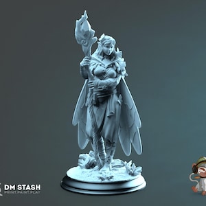 Könnte beinhalten: Eine detaillierte, hellfarbene Figur eines weiblichen Fantasy-Charakters, der einen Stab mit kristallartiger Spitze hält. Die Figur trägt einen fließenden Umhang und eine Rüstung und steht auf einem kreisförmigen Sockel mit floralen Akzenten. Text: "DM STASH PRINT. PAINT. PLAY."