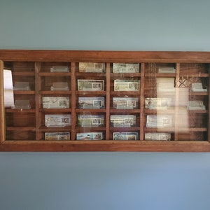 May include: A wooden display case with glass doors and shelves for holding small items. The case has a dark brown finish and is mounted on a wall.