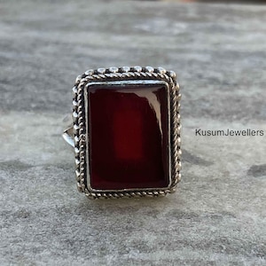 May include: A silver ring with a rectangular red gemstone set in a beaded border.