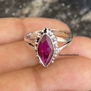 Może przedstawiać: Srebrny pierścionek z rubinem w kształcie markizy osadzonym w ozdobnej srebrnej oprawie. Pierścionek ma delikatny, skręcony pasek.