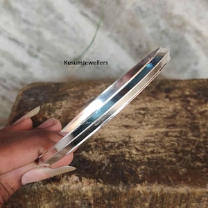 May include: A silver bangle bracelet with a textured, faceted design. The bracelet is approximately 1/2 inch wide.