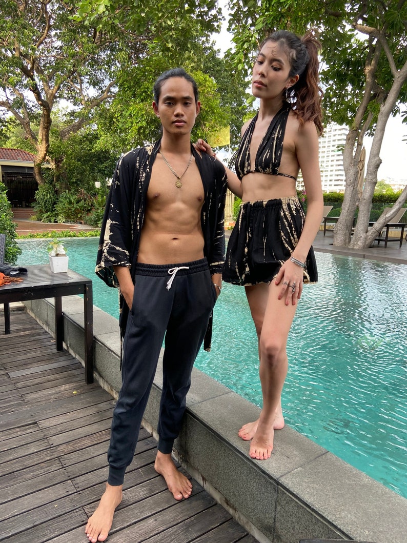 May include: A couple wearing black and white tie-dye clothing. The woman is wearing a halter top and shorts. The man is wearing a long-sleeved shirt and pants. They are standing by a pool.