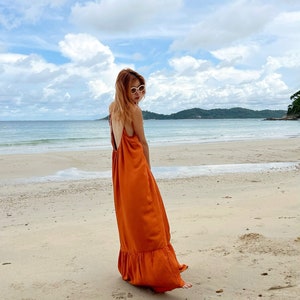 Shop burnt orange maxi dress with a low back and ruffled hem. The dress is worn on a sandy beach with the ocean and sky in the background.
