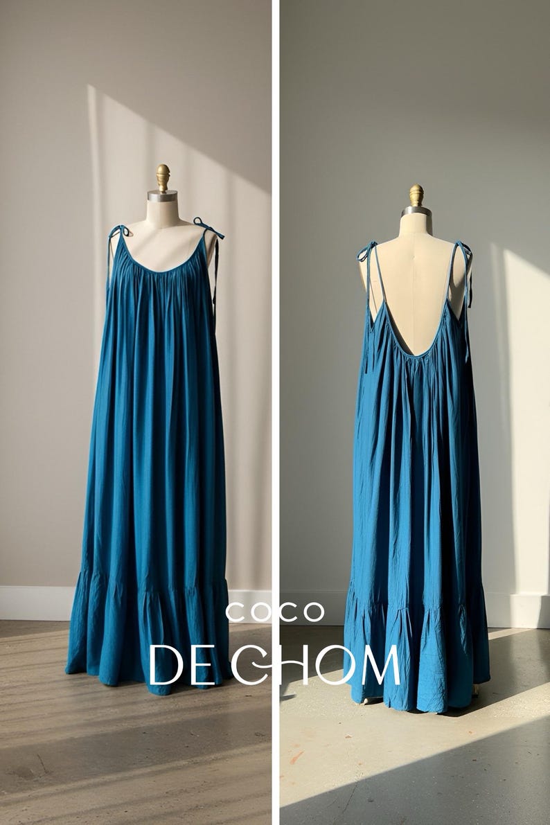 Back view of a blue turquoise open back maxi dress with tie shoulders and a flowing oversized fit, worn barefoot on the beach.