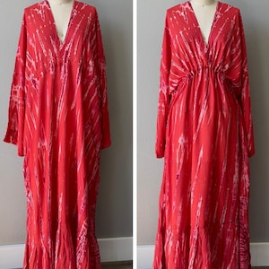 A red maxi dress with a V-neckline and long sleeves. The dress has a cinched waist and a flowing skirt.