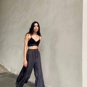 Puede incluir: Una mujer con un bralette de encaje negro y pantalones anchos de color gris oscuro con un patr&oacute;n de tie-dye.