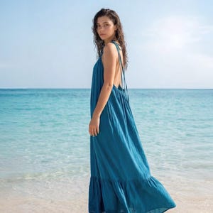 Side view of a blue turquoise maxi dress with open back, tie shoulders, and ruffle hem, styled as a flowy beach and resort dress.