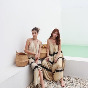 May include: Two women wearing long, flowy, tie-dye dresses with black stripes. They are sitting on a white ledge with a woven basket beside them. The background is a white wall and a light blue surface.