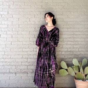 May include: A long, purple and black tie-dye maxi dress with a V-neckline and 3/4 sleeves. The dress has a tie at the waist and is made of a soft, flowing fabric.