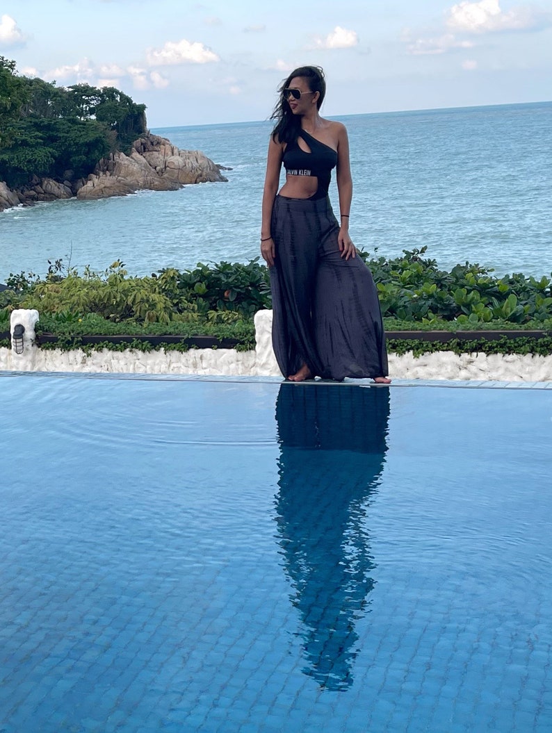 Puede incluir: Una mujer con un traje de ba&ntilde;o negro de una pieza con recortes y un logotipo de Calvin Klein se encuentra junto a una piscina. La piscina est&aacute; rodeada por un borde de azulejos blancos y exuberante vegetaci&oacute;n. La mujer lleva gafas de sol y tiene el pelo largo y oscuro.