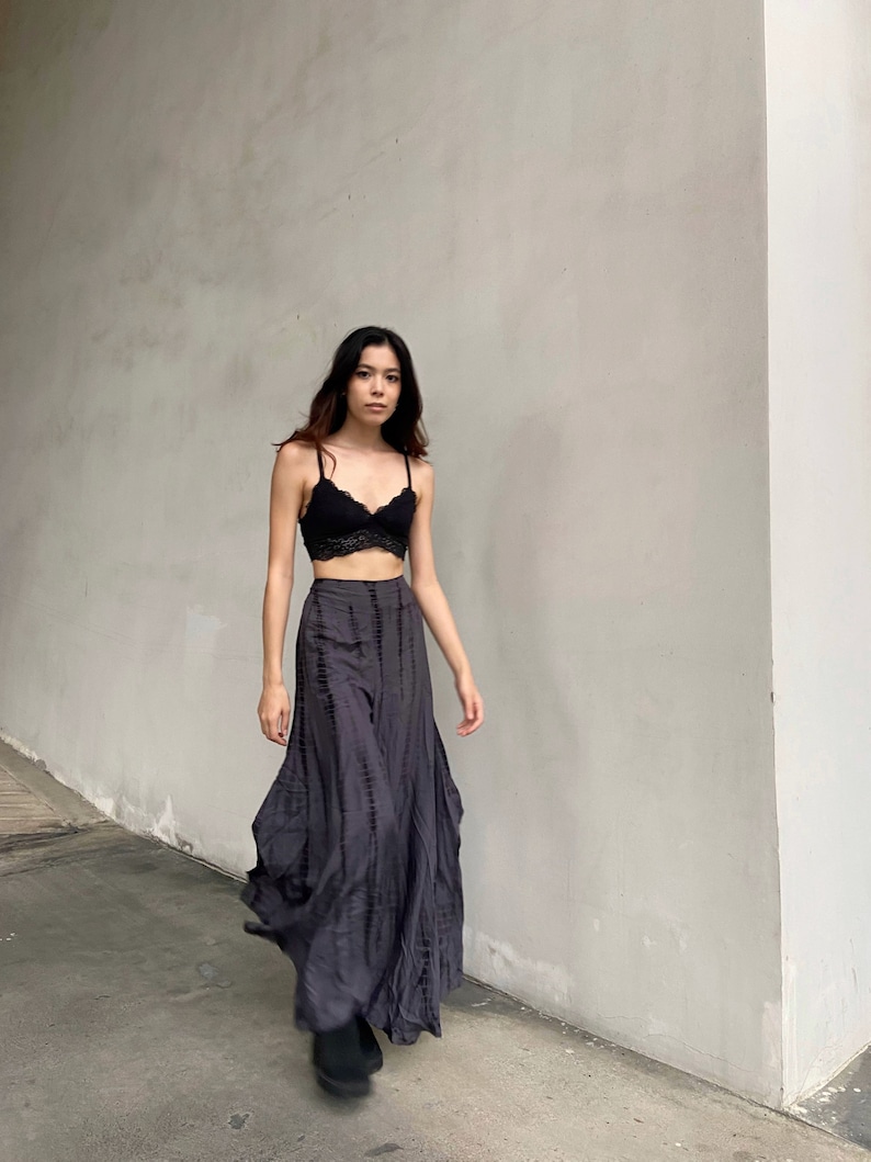 Puede incluir: Una mujer con un bralette de encaje negro y una falda larga y fluida de color gris con un patr&oacute;n de tie-dye. Est&aacute; caminando hacia la c&aacute;mara.