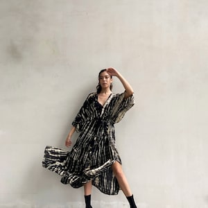 May include: A woman wearing a black and white tie-dye maxi dress with a long sleeve and a wrap style. She is wearing black ankle boots and has her hair pulled back.