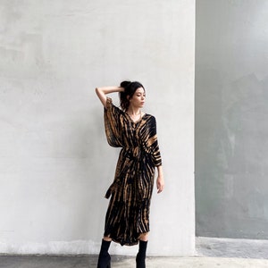 May include: A woman wearing a long, black and brown tie-dye dress with a long sleeve and a tie at the waist. She is wearing black ankle boots.