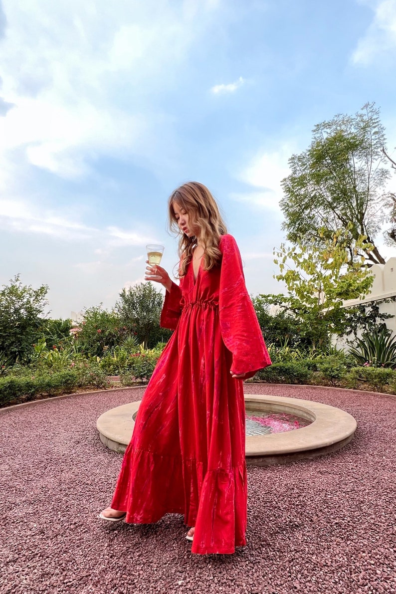 A red maxi dress with a V-neckline and long sleeves. The dress has a cinched waist and a flowing skirt.