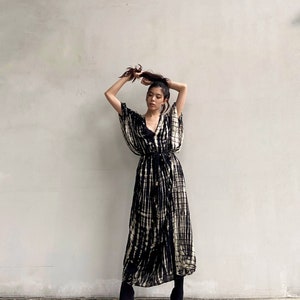 May include: A woman wearing a black and white tie-dye maxi dress with a long-sleeved, wrap-style top and a cinched waist. She is wearing black ankle boots.