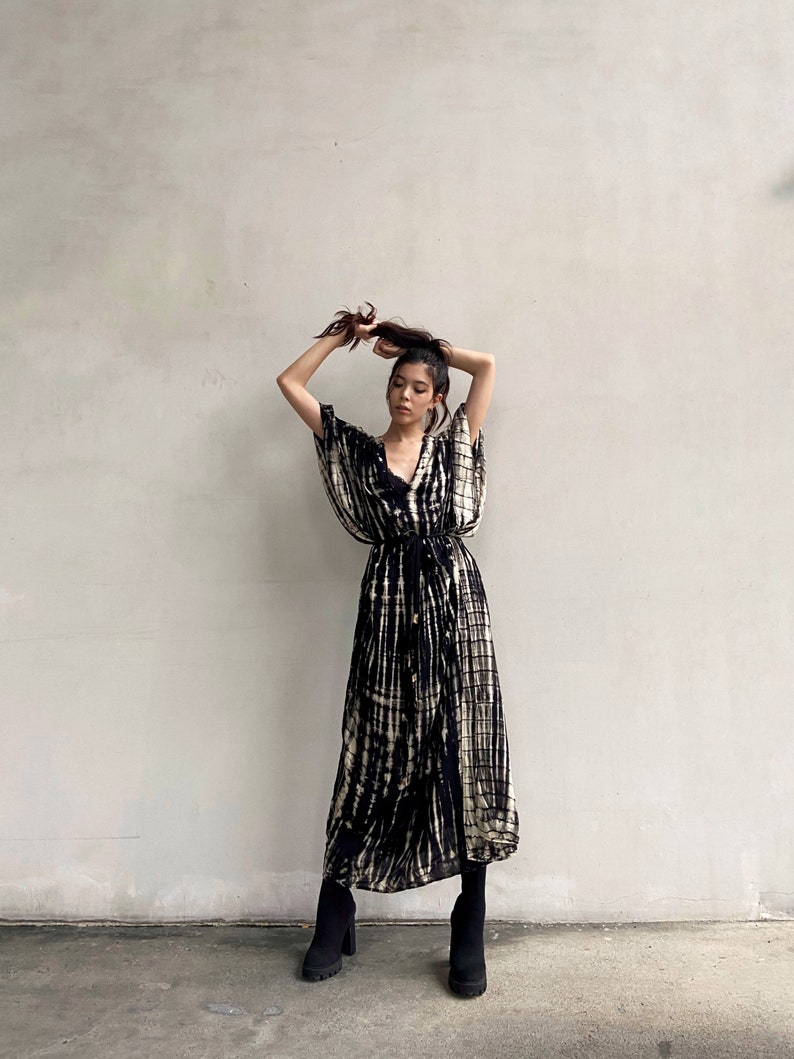 May include: A woman wearing a black and white tie-dye maxi dress with a long-sleeved, wrap-style top and a cinched waist. She is wearing black ankle boots.