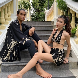 May include: A couple wearing matching black and white tie-dye clothing. The woman is wearing a halter top and shorts. The man is wearing a long-sleeved shirt and pants. They are sitting on a set of stairs.