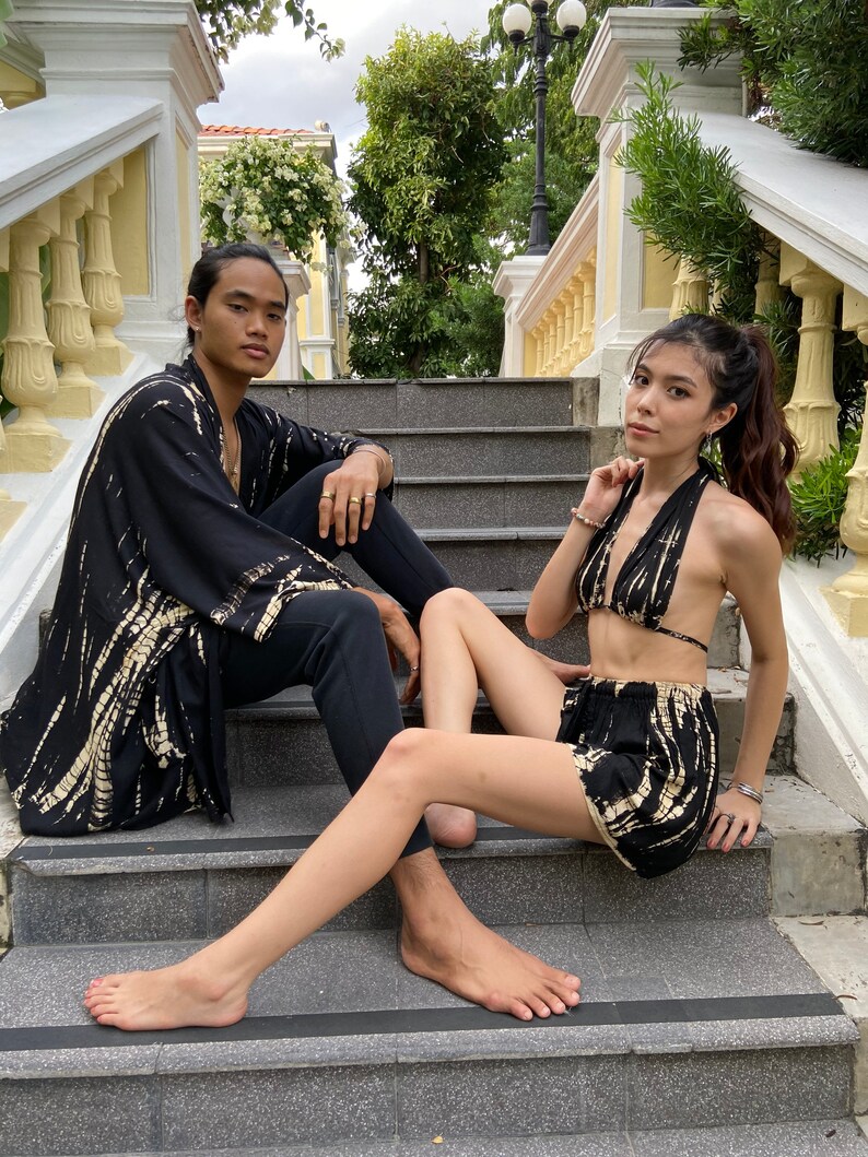 May include: A couple wearing matching black and white tie-dye clothing. The woman is wearing a halter top and shorts. The man is wearing a long-sleeved shirt and pants. They are sitting on a set of stairs.