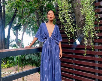 May include: A woman wearing a long, blue tie-dye maxi dress with a deep V-neckline and short sleeves. The dress has a tie at the waist and is flowing in the breeze.