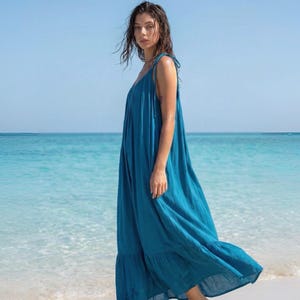 Side view of a blue turquoise maxi dress with open back, tie shoulders, and ruffle hem, styled as a flowy beach and resort dress.
