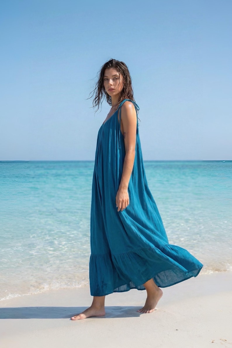 Side view of a blue turquoise maxi dress with open back, tie shoulders, and ruffle hem, styled as a flowy beach and resort dress.