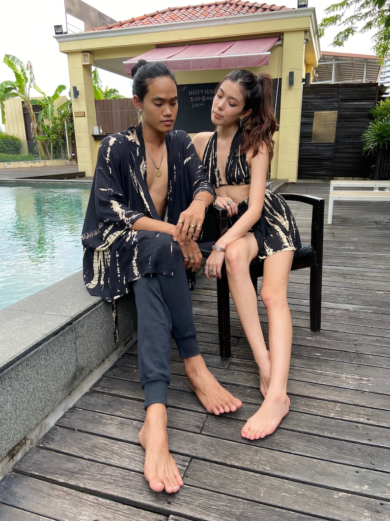 May include: A couple wearing matching black and white tie-dye clothing. The man is wearing a long-sleeved shirt and black pants. The woman is wearing a halter top and a short skirt. They are sitting on a wooden deck by a pool.