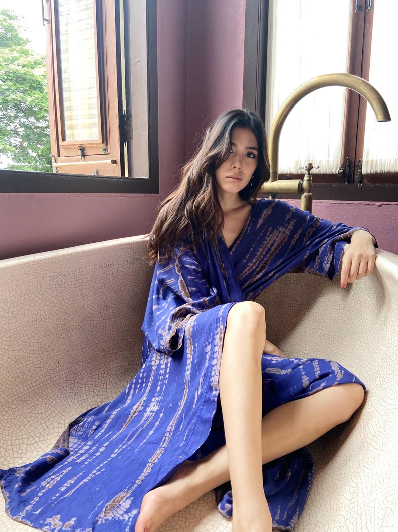 May include: A woman wearing a long, blue and purple tie-dye robe with a V-neckline. The robe has a flowing, relaxed fit and is made of a soft, lightweight fabric.