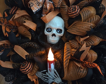 May include: A Halloween wreath with a skull centerpiece, orange and black ribbons, and decorative pumpkins. The wreath includes a battery-operated candle held by a skeleton hand. The ribbons have the words "Happy Halloween" and spiderwebs.