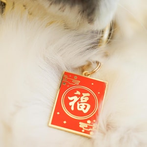 Peut inclure: Un chien blanc portant un collier en or avec une &eacute;tiquette rouge et or qui dit "福" en caract&egrave;res chinois.