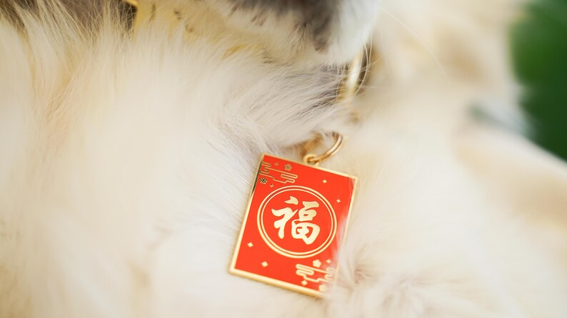 Peut inclure: Un chien blanc portant un collier en or avec une &eacute;tiquette rouge et or qui dit "福" en caract&egrave;res chinois.