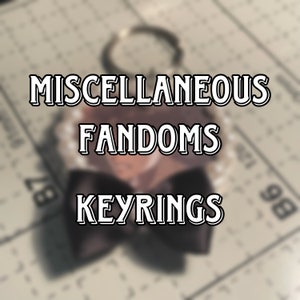May include: A black and white keychain with a bow and the text "MISCELLANEOUS FANDOMS KEYRINGS" on a white background.