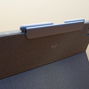 Op de afbeelding: Een donkergrijze iPad-hoes van stof met een ingebouwde penhouder. De hoes heeft een Logitech-logo op de achterkant.