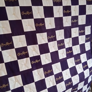 May include: A purple and white checkered fabric quilt with the words "Crown Royal" embroidered in gold on each square.